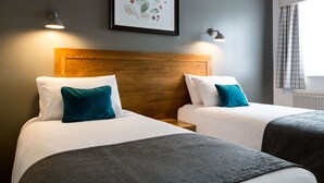 Ett hotellrum med två sängar, en sänggavel i trä och ett inramat konstverk på väggen.