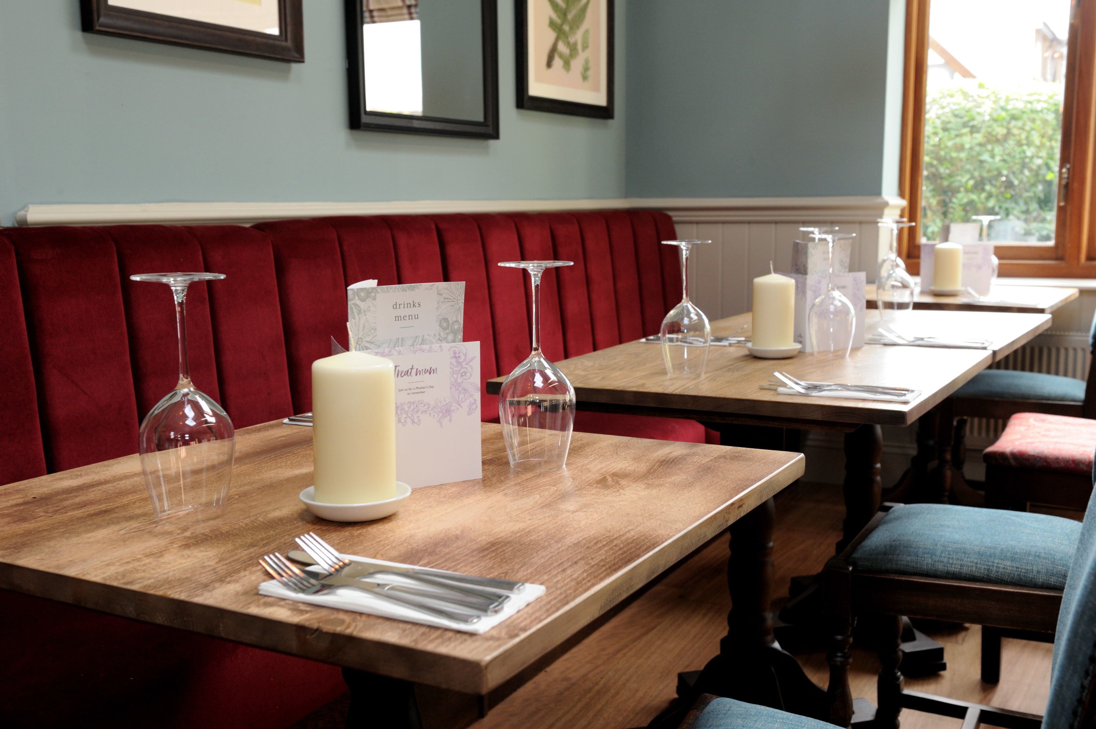 A restaurant with wooden tables, red upholstered booths, and clear glass candle holders.