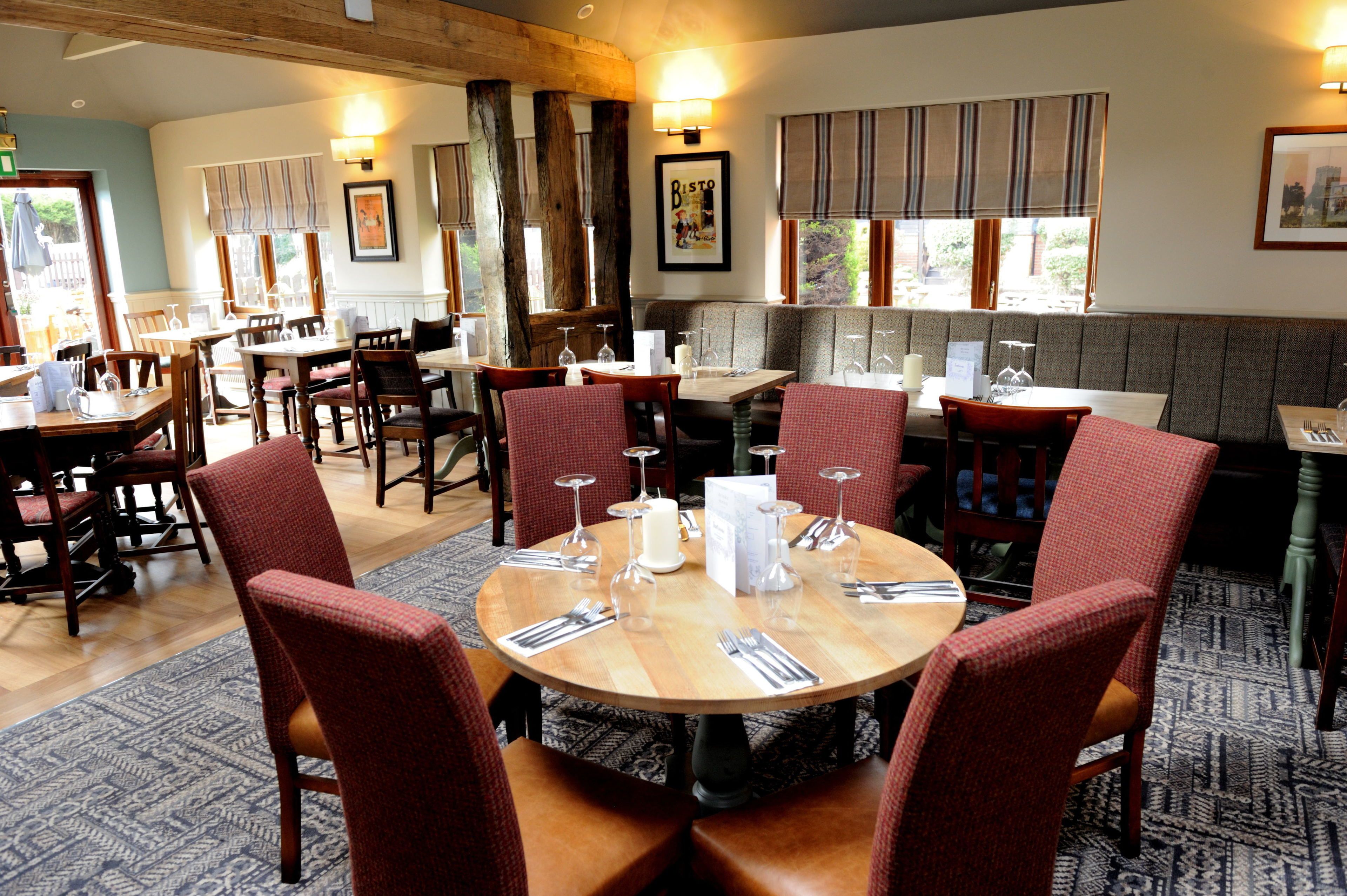 A restaurant with round tables, red upholstered chairs, and wooden beams on the ceiling.