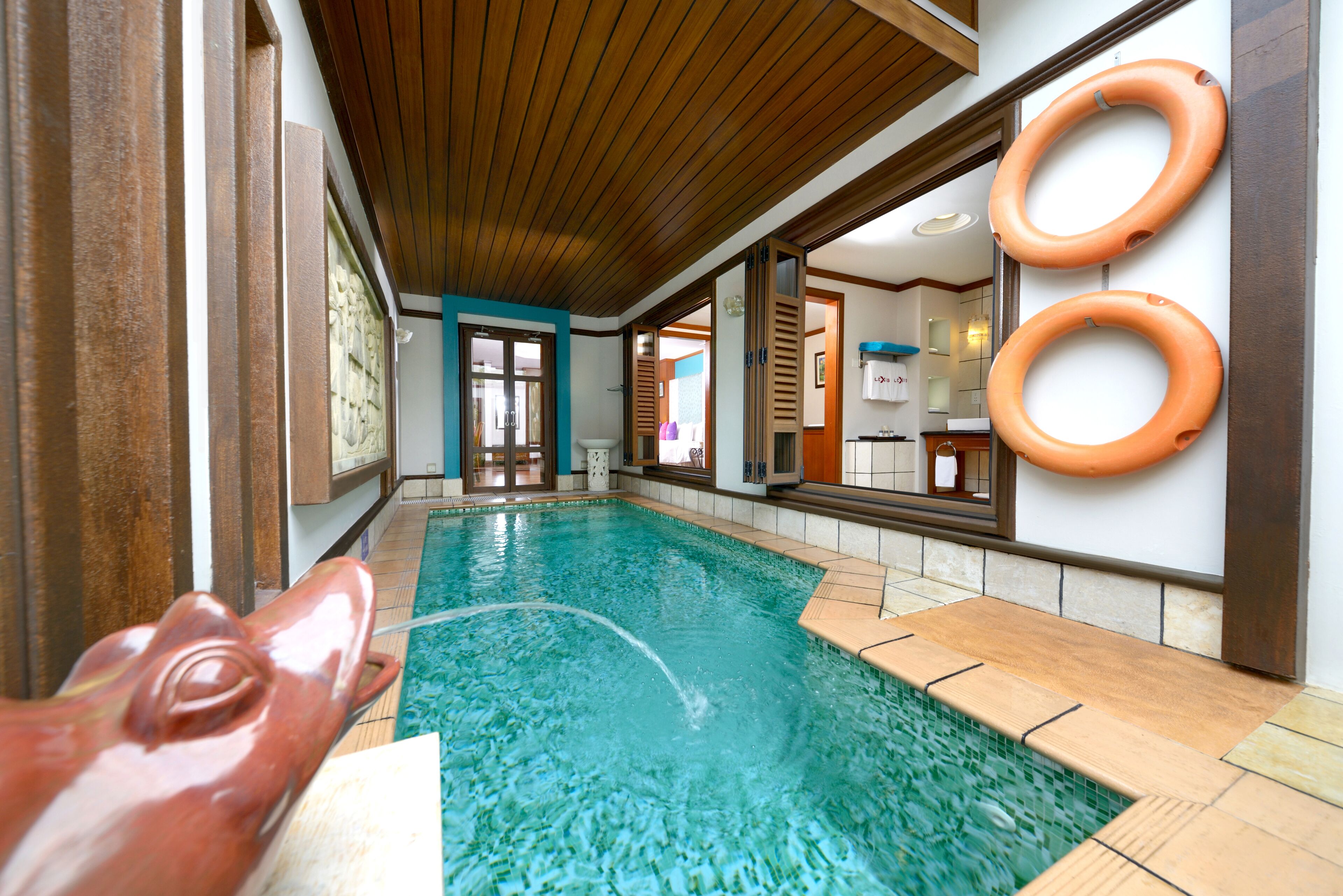 An indoor swimming pool with clear water, wooden ceiling, and two orange lifebuoys on the wall.