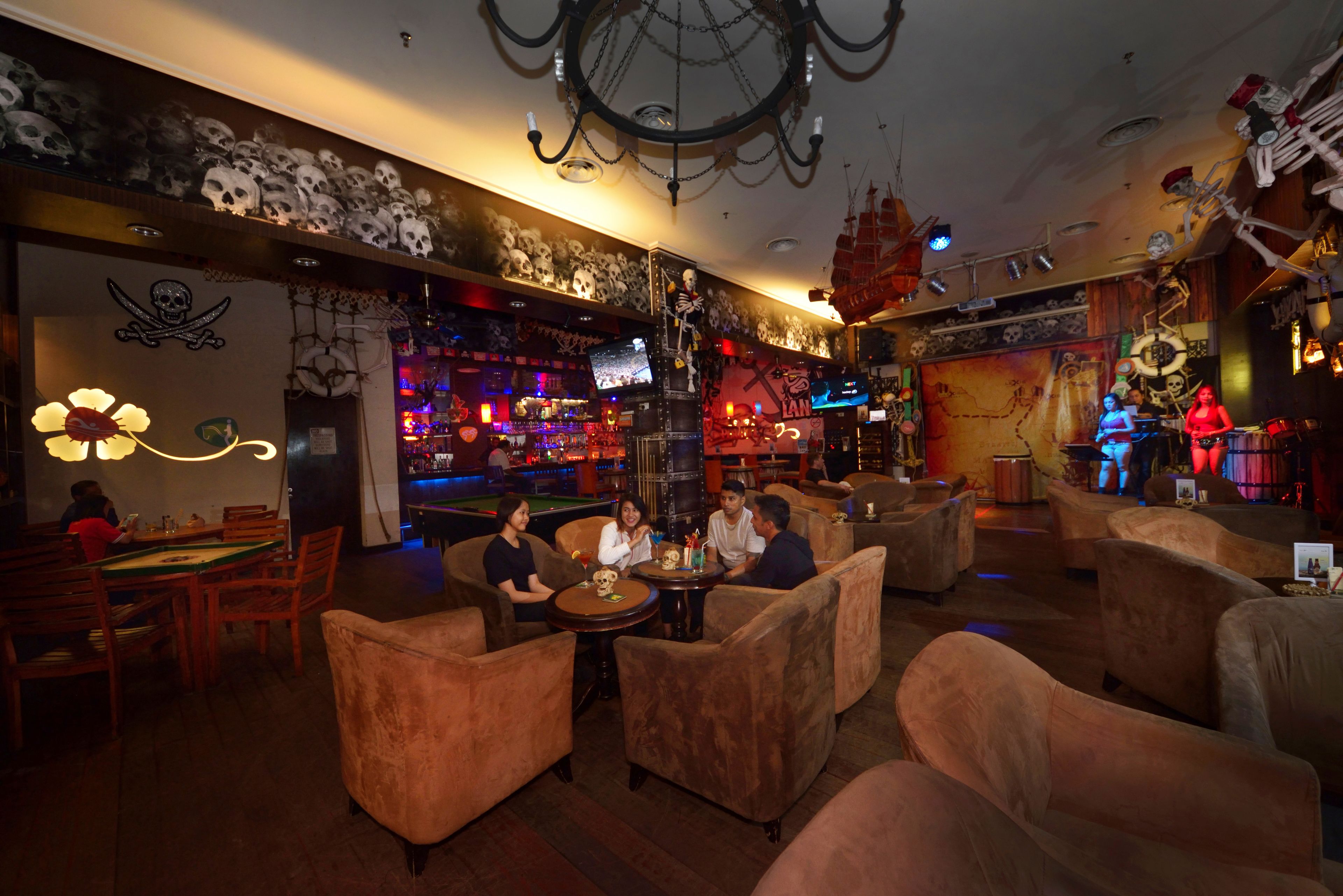 A bar area with sofas and a pool table, decorated with skulls and pirate-themed items.