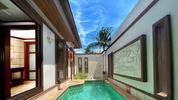 A swimming pool with clear water, surrounded by a tiled deck and a white wall with a relief sculpture.
