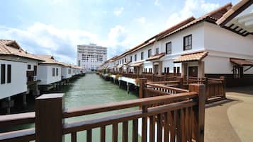 Un paseo junto al canal con barandas de madera, edificios blancos con tejados de azulejos y un cielo despejado.