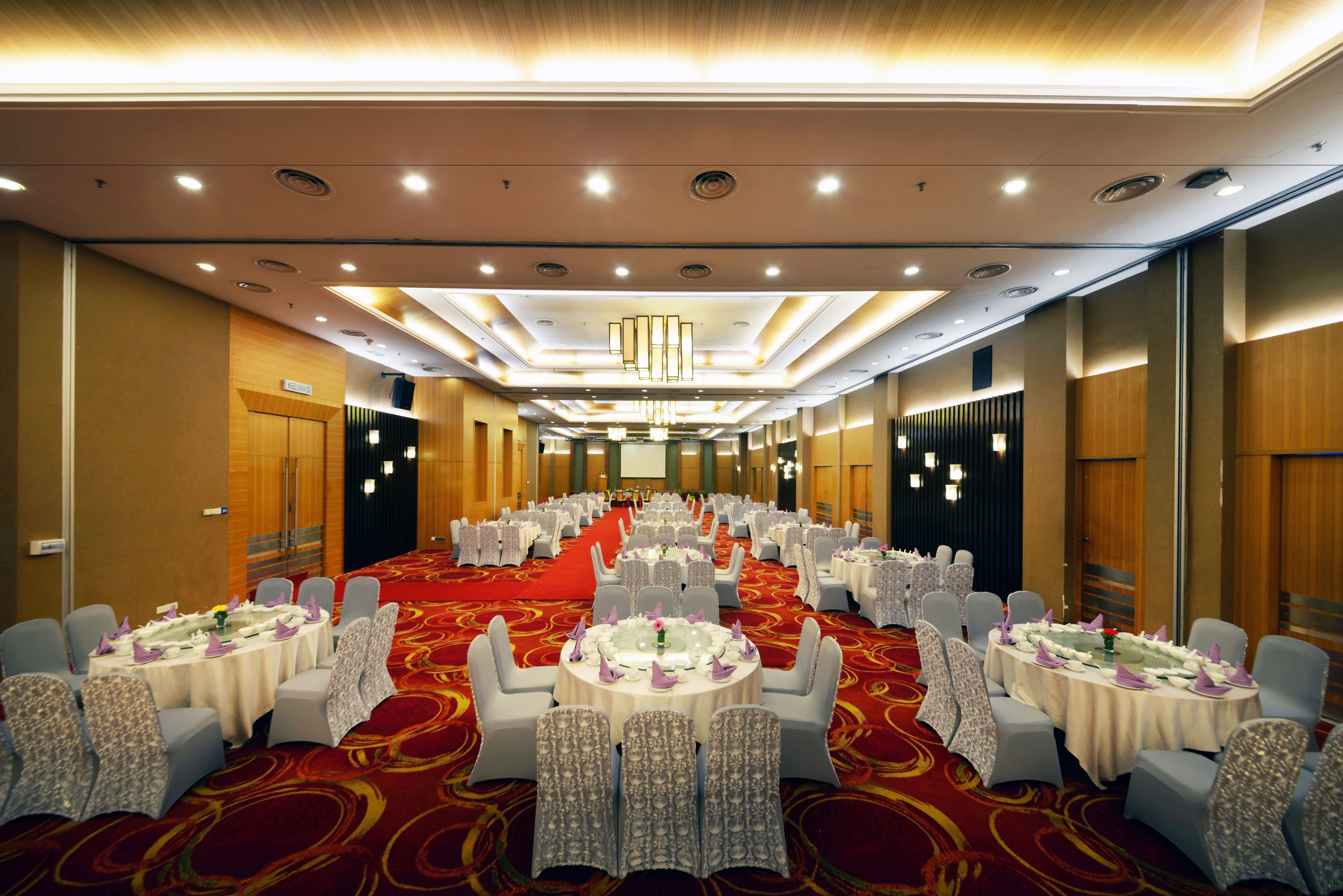 A banquet hall with round tables, chairs, and a red carpet.