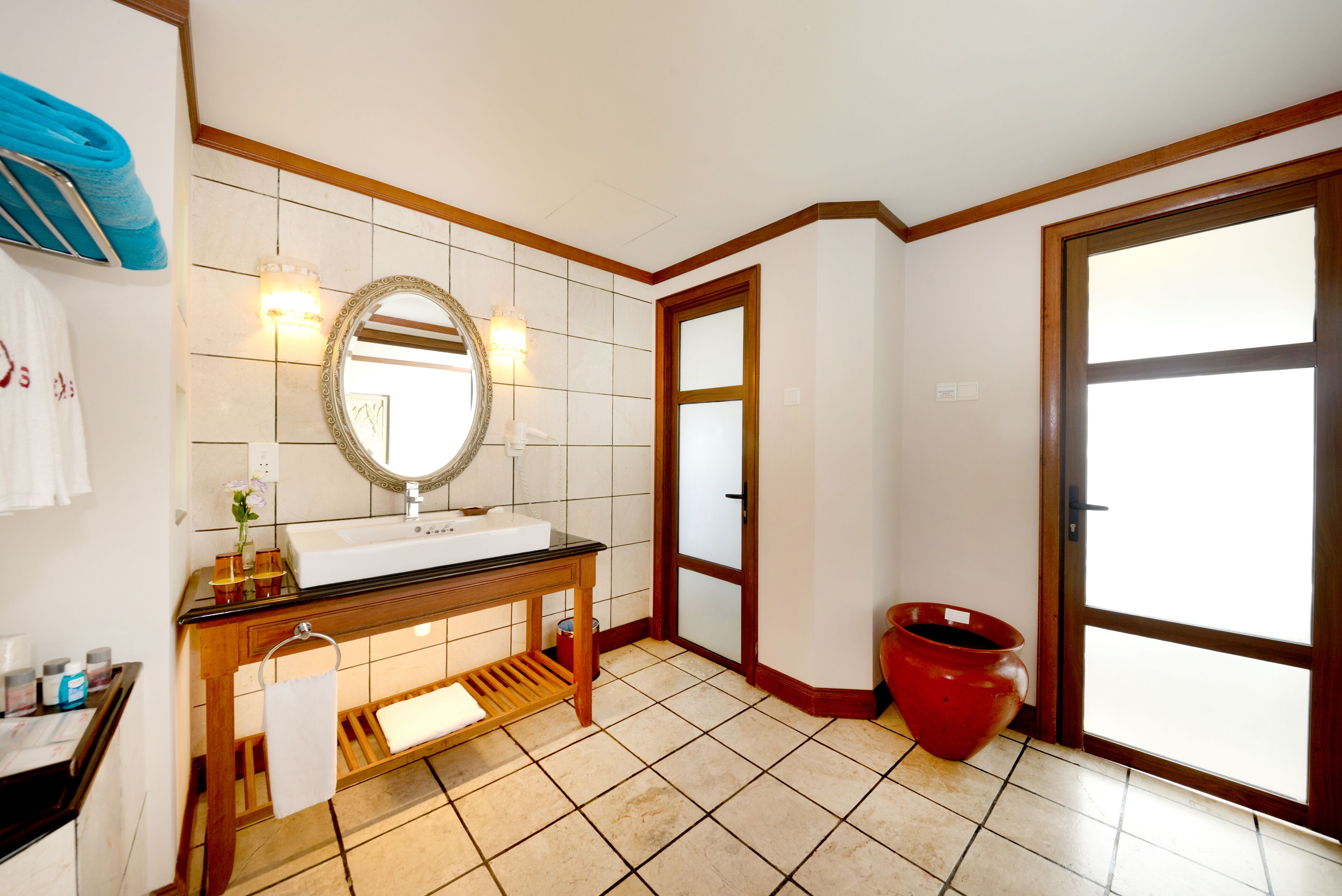 A bathroom with a sink, mirror, and a red vase.