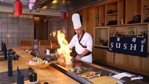 A chef cooking at a sushi bar with a fire feature.