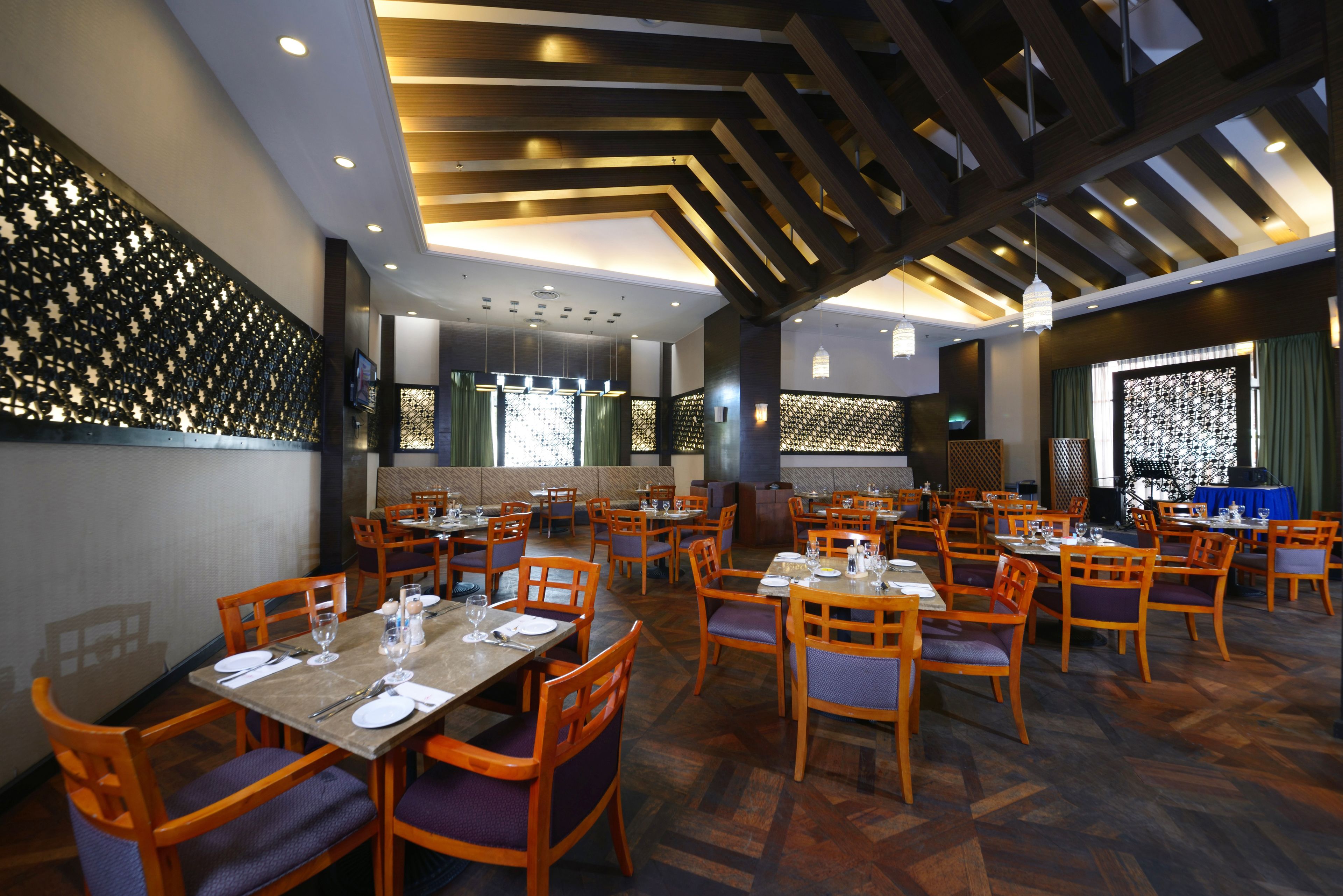 A restaurant with multiple dining tables and chairs, a patterned wall, and a wooden ceiling.