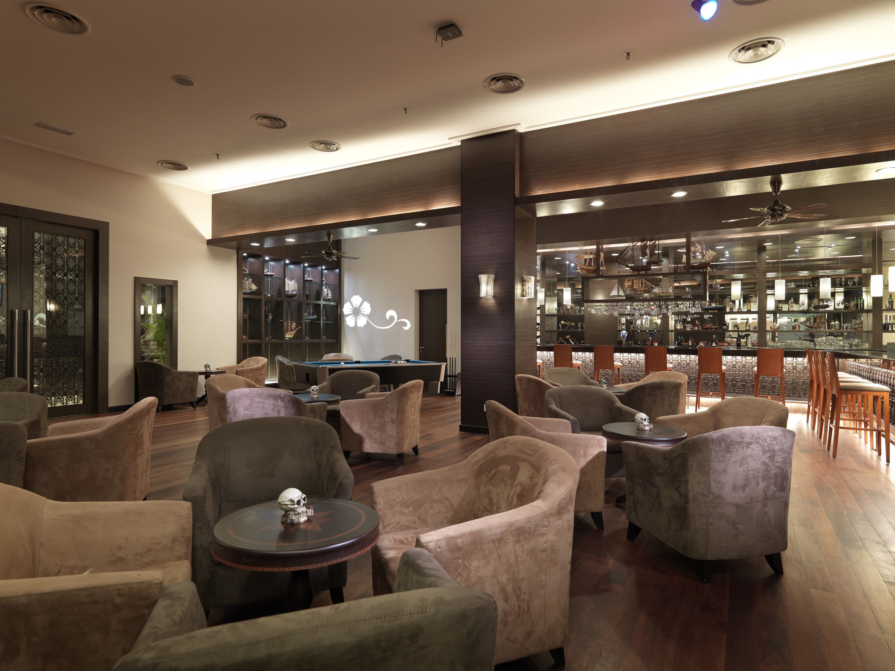 A modern lounge area with plush seating, a pool table, and a bar with a variety of bottles and glasses.