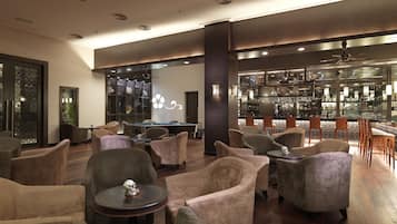 A modern lounge area with plush seating, a pool table, and a bar with a variety of bottles and glasses.