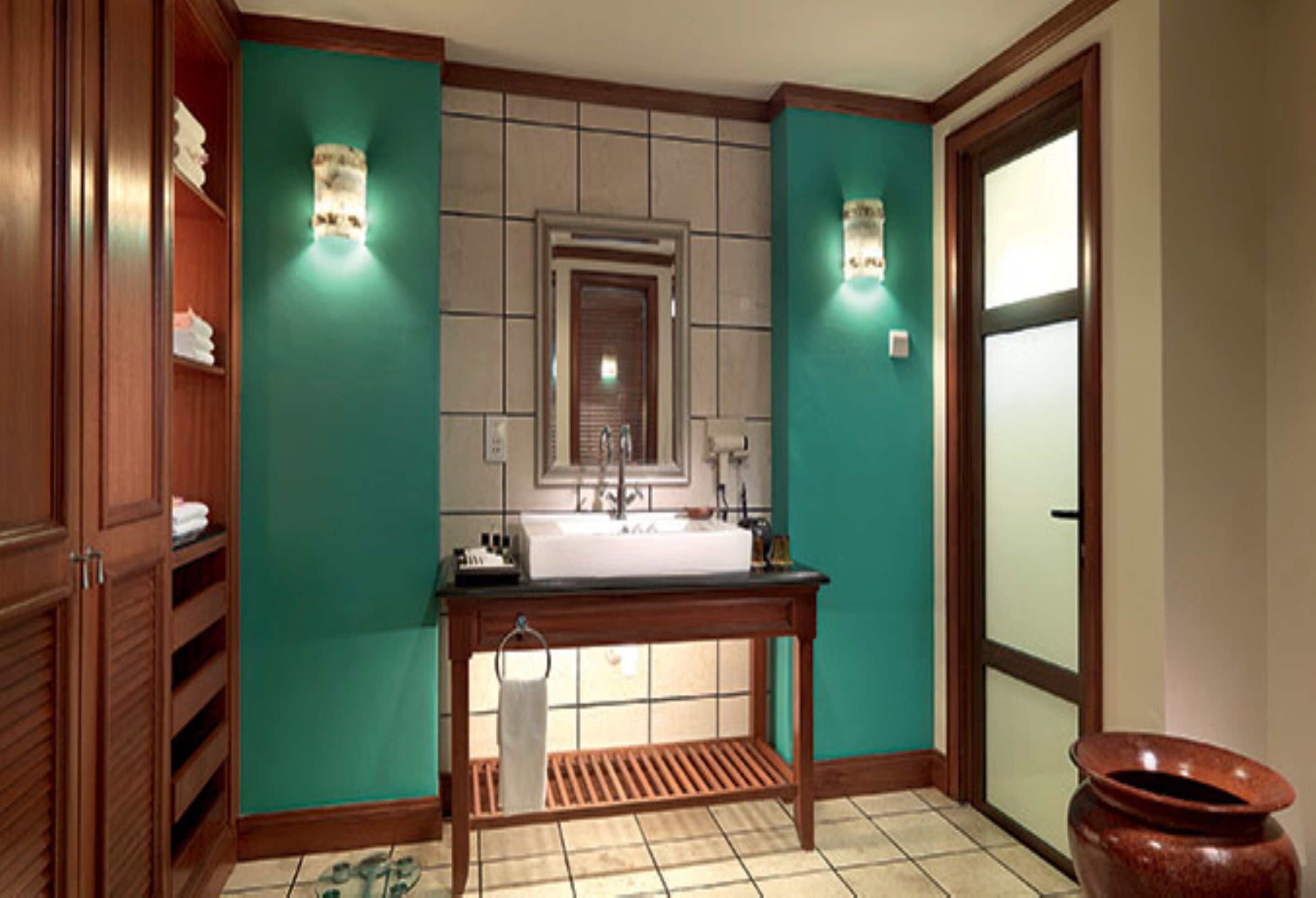 Un baño con un tocador de madera, un lavabo y un espejo. Hay dos luces fijadas a la pared y un perchero para toallas.