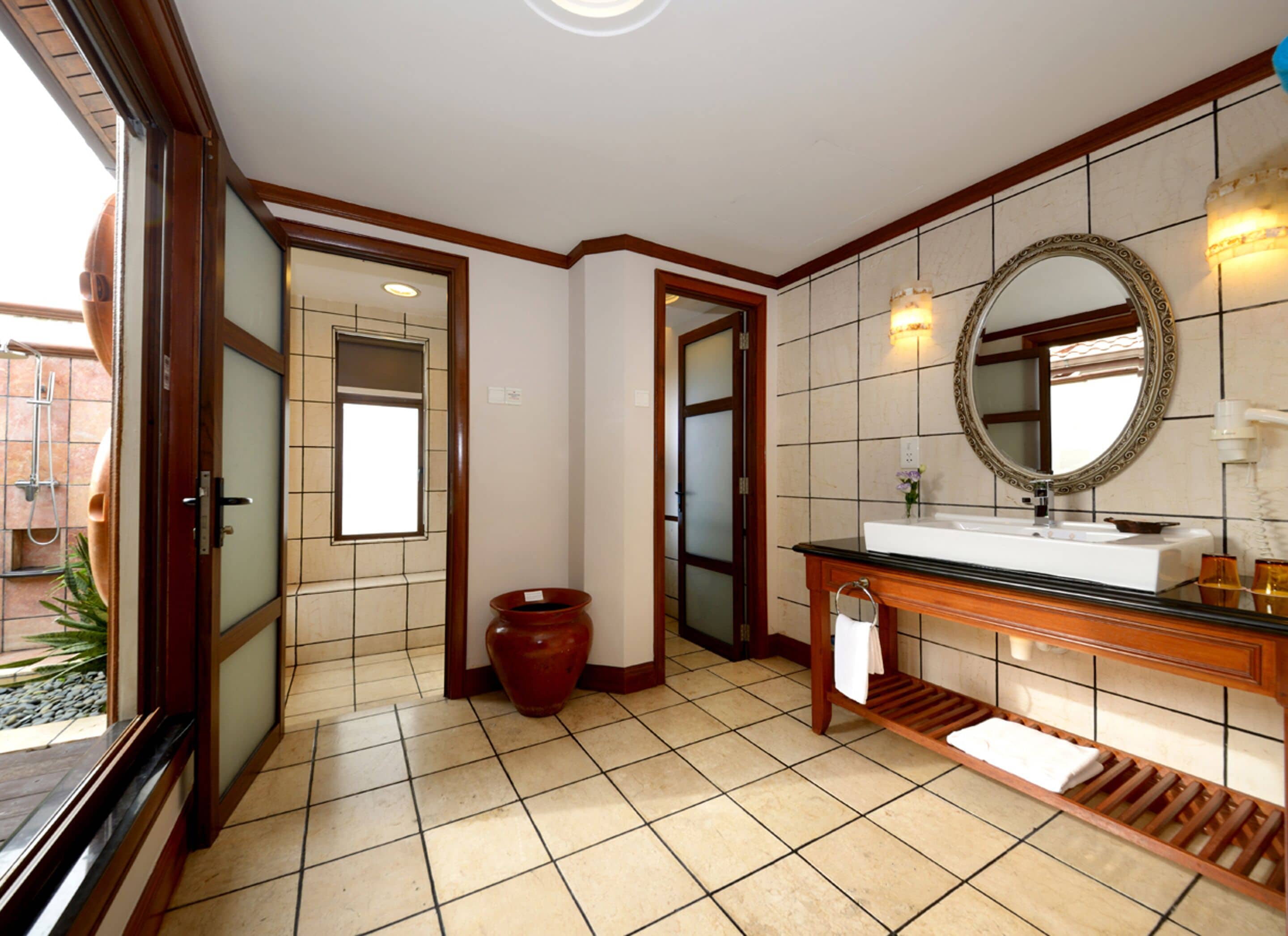 Un baño espacioso con un espejo grande, un tocador de madera y piso de baldosas.