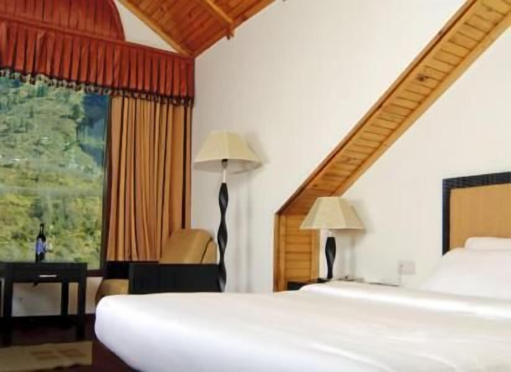 Una habitación de hotel con una cama, dos lámparas, una silla y un cuadro en la pared.