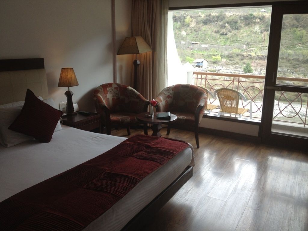 Habitación de hotel con cama, dos sillones, una mesita y balcón con vistas al campo.