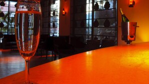 A glass of champagne on a bar counter with a view of the interior of a restaurant, including a window with decorative items and a bottle of champagne. - Mastiff Grand Manali (Manali)