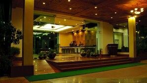 A hotel lobby with a reception desk, a staircase leading to the upper floor, and a green carpeted area. - Mastiff Grand Manali (Manali)