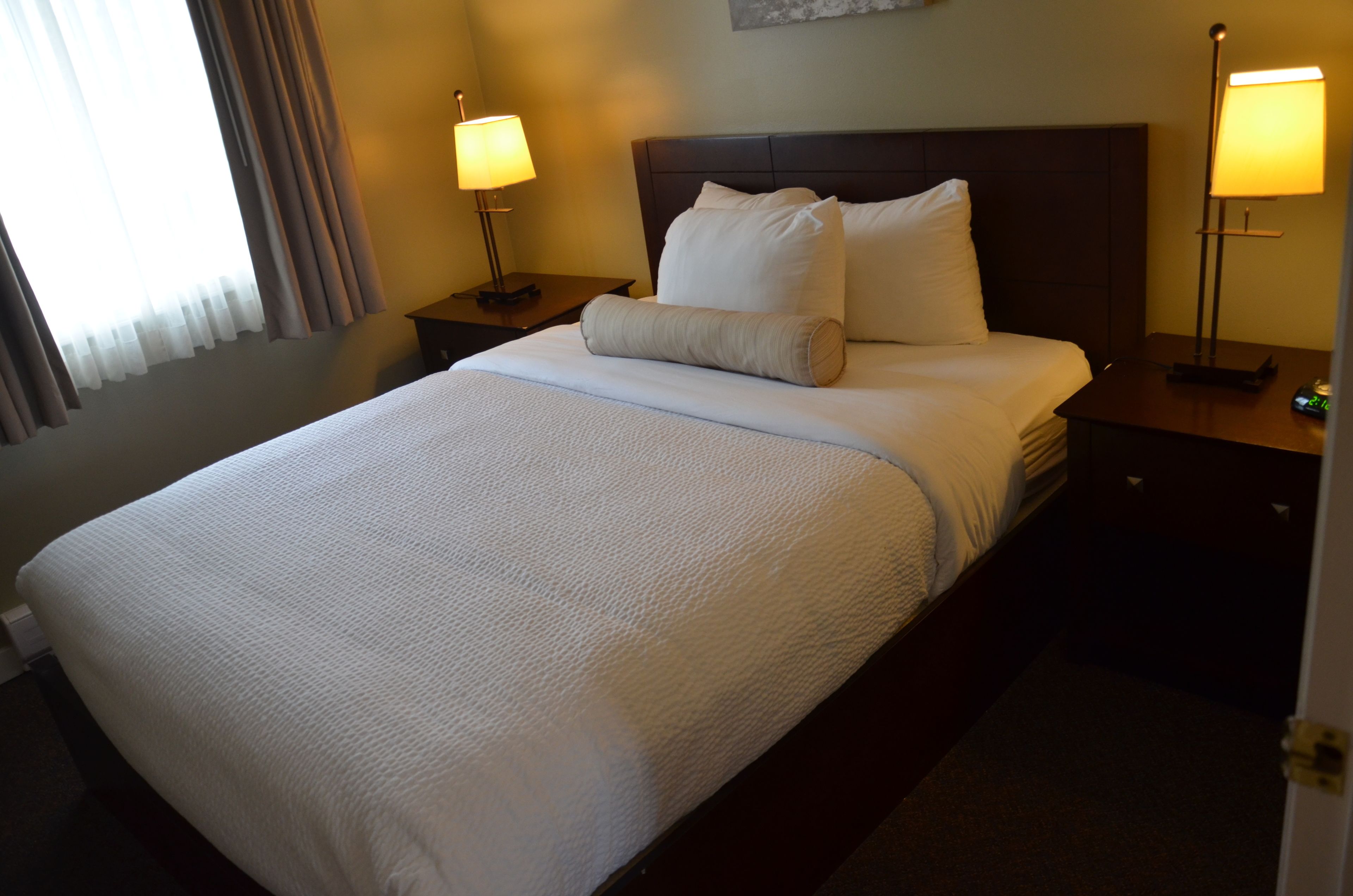 A hotel room with a large bed, two bedside tables, and two lamps.