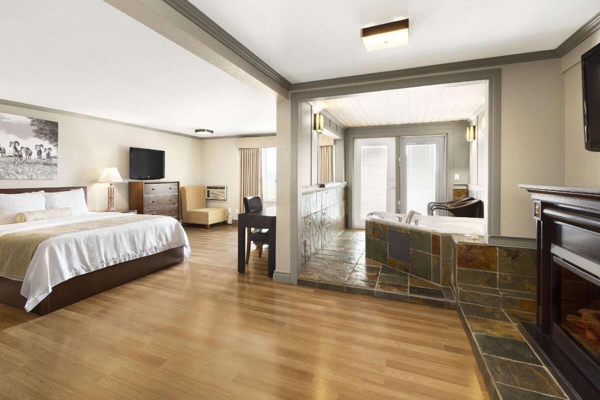 A hotel room with a bed, desk, chair, and a fireplace.