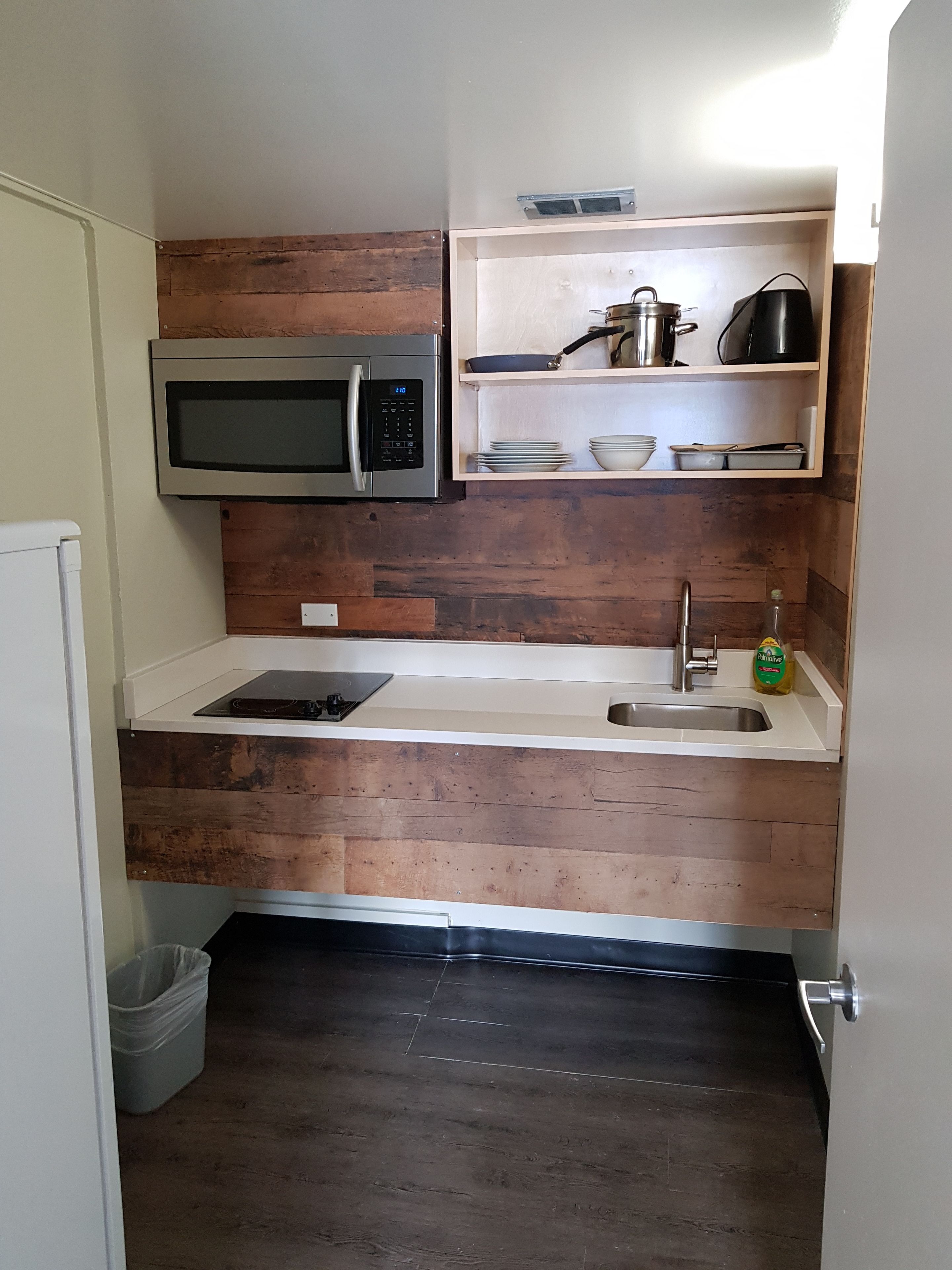 Een kleine keuken met een magnetron, spoelbak en een houten achterwand.