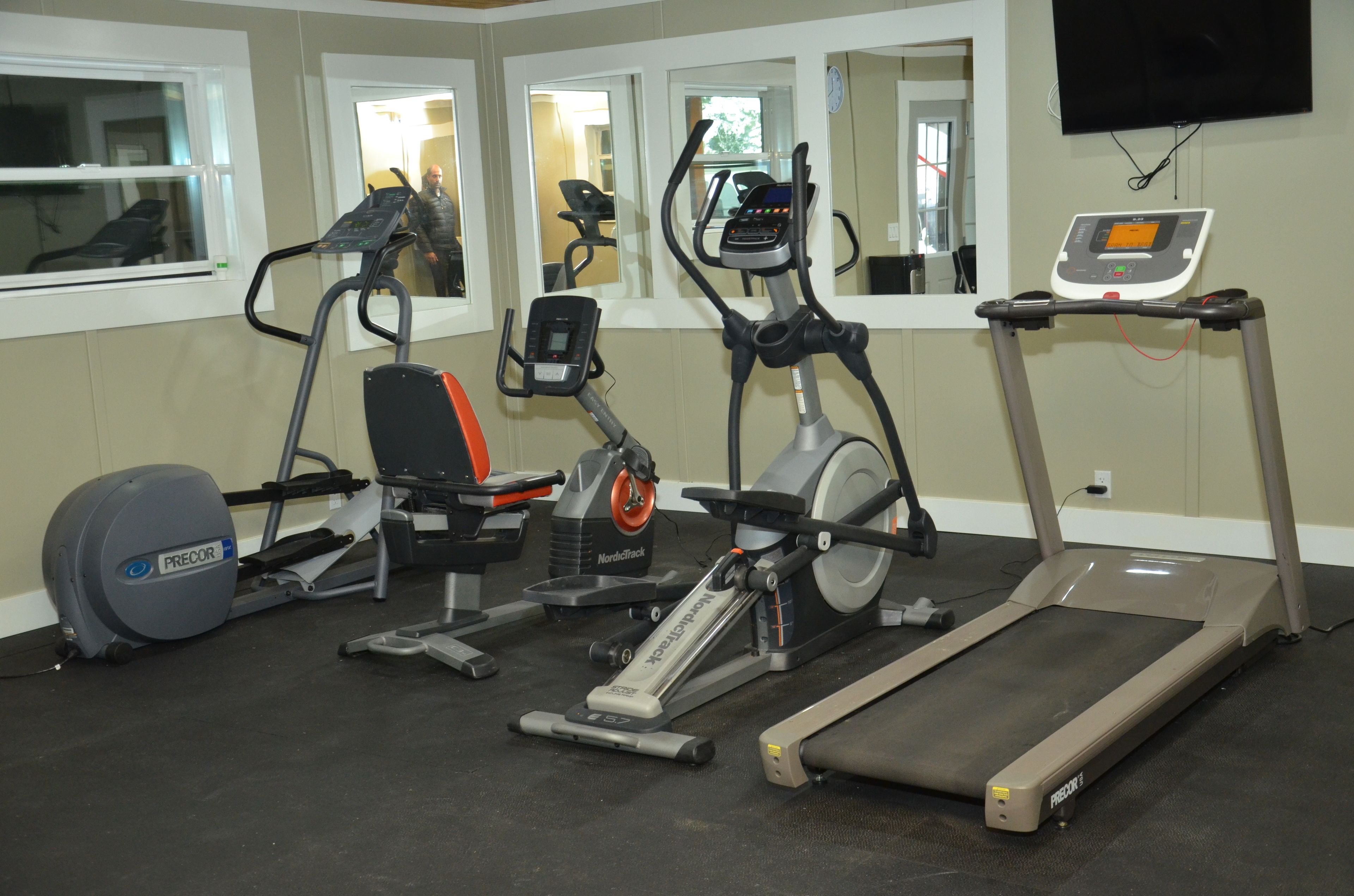 Ein Fitnessraum mit verschiedenen Trainingsgeräten, darunter Laufbänder, ein Crosstrainer und ein Ergometer.