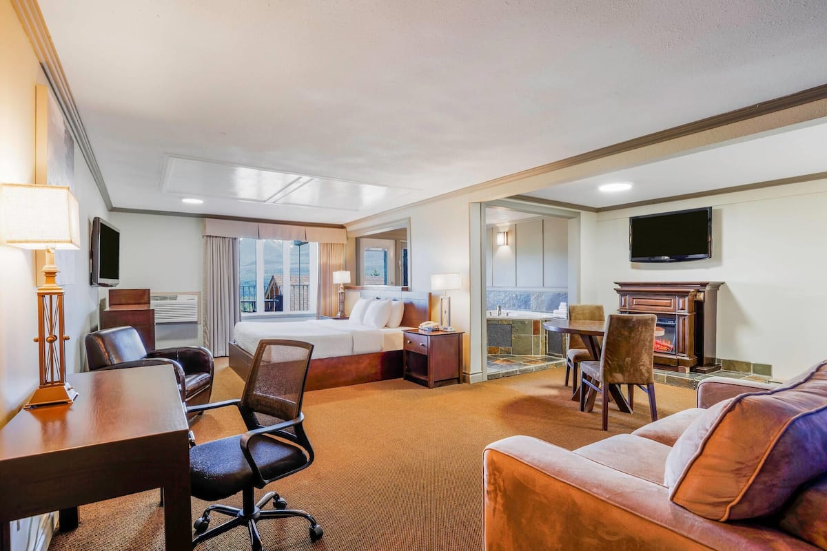 A hotel room with a bed, a desk, a sofa, a TV, and a fireplace.