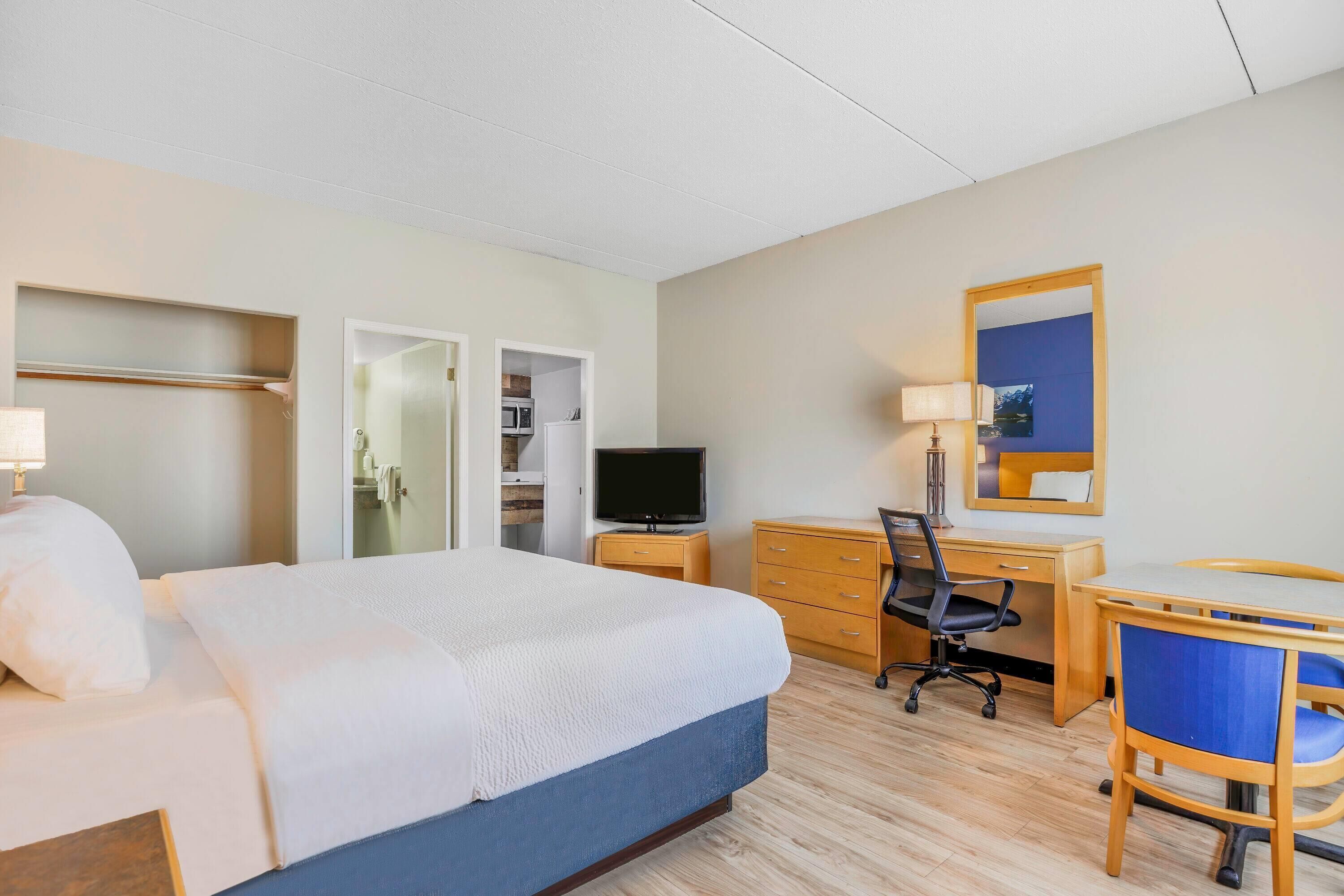 Ein Hotelzimmer mit einem Bett, einem Schreibtisch, einem Stuhl, einem Fernseher und einem Kleiderschrank.