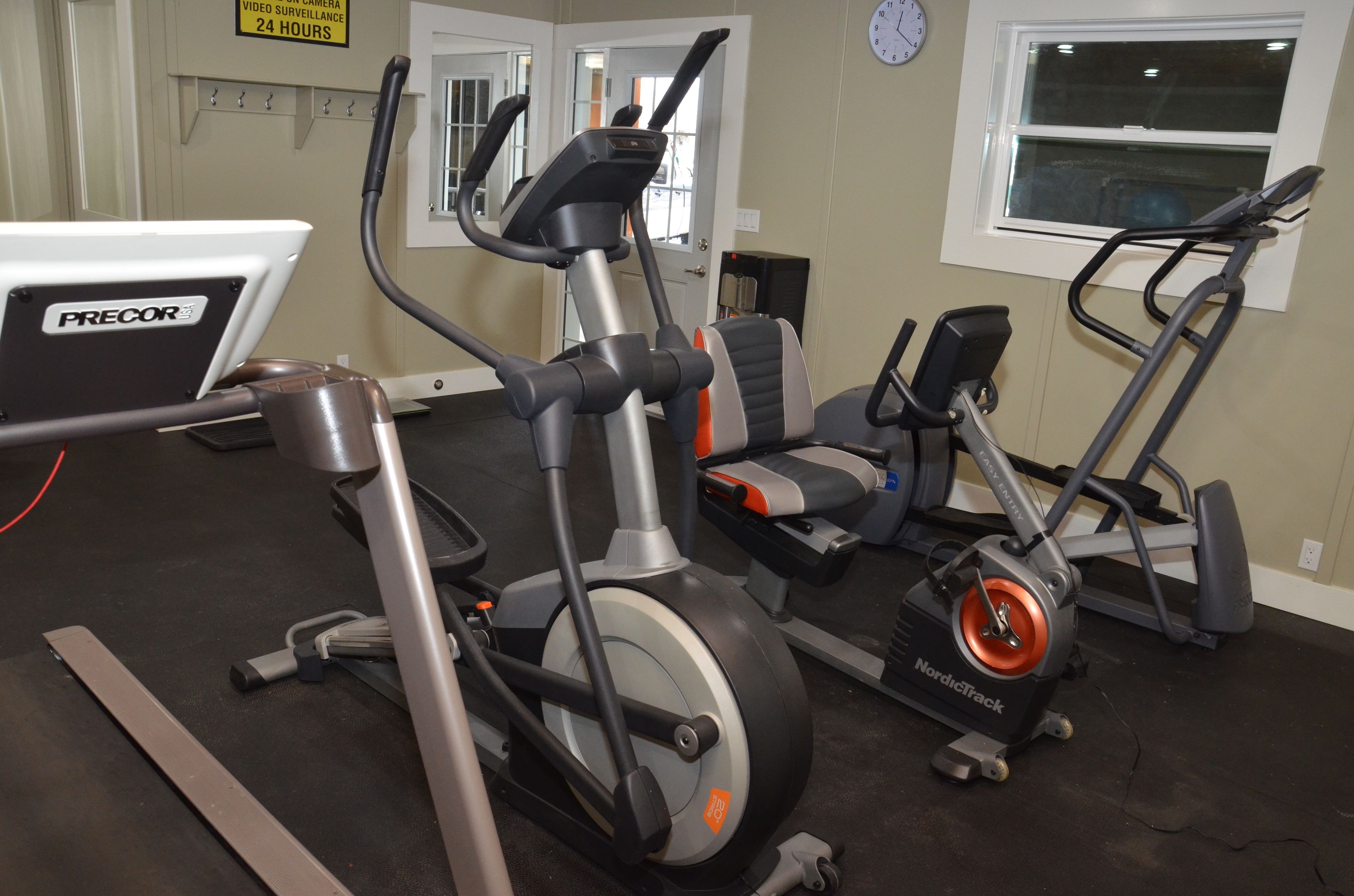 A gym with various exercise equipment including a PRECOR elliptical, a NordicTrack bike, and a treadmill.