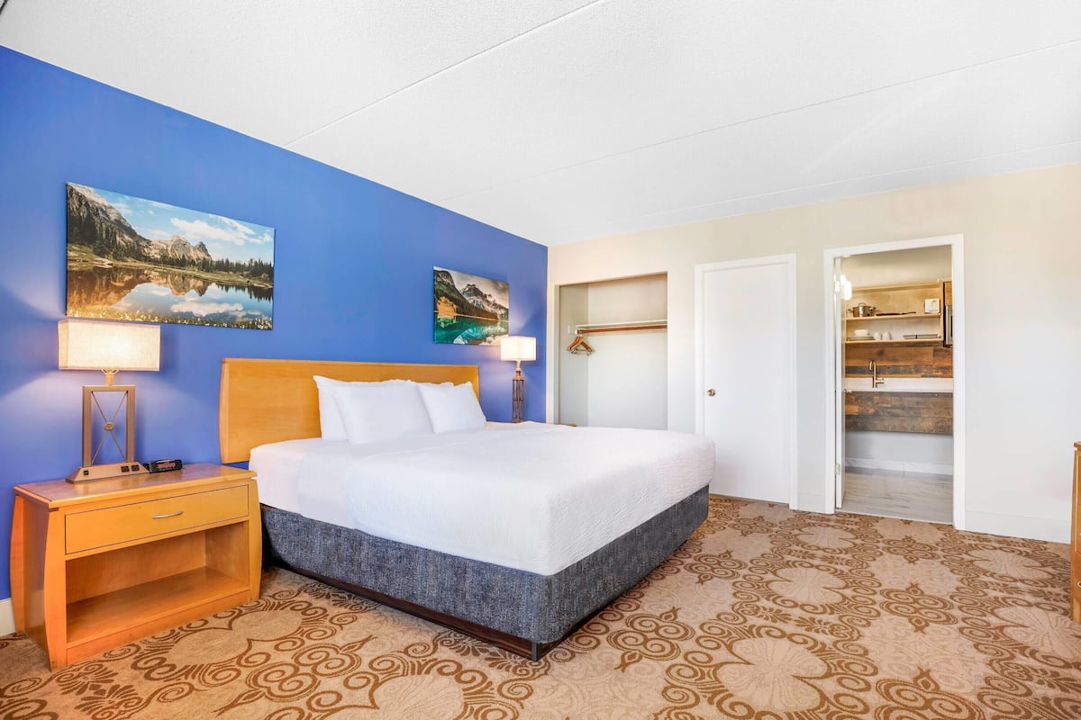 A hotel room with a large bed, two bedside tables with lamps, a wardrobe, and a bathroom visible through an open door.