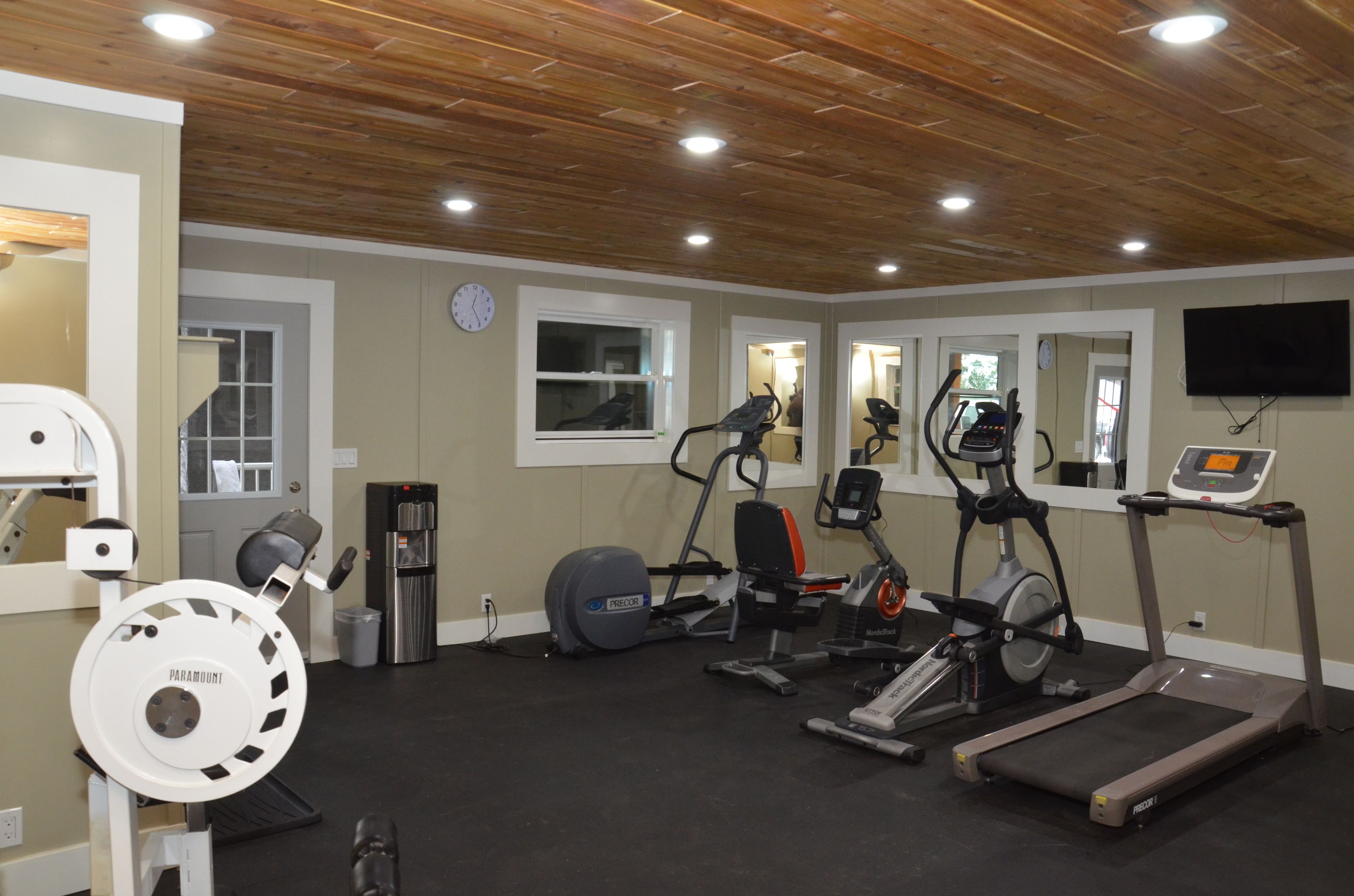 Une salle de sport à domicile équipée d’un tapis de course, d’un vélo elliptique, d’un vélo d’appartement et d’une machine de musculation.