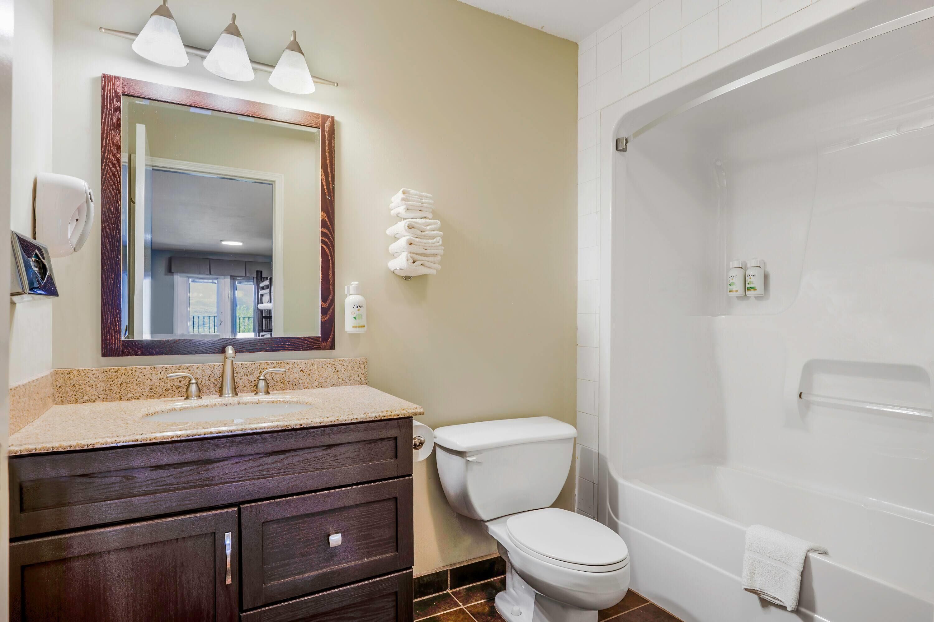 A bathroom with a sink, mirror, toilet, and bathtub.