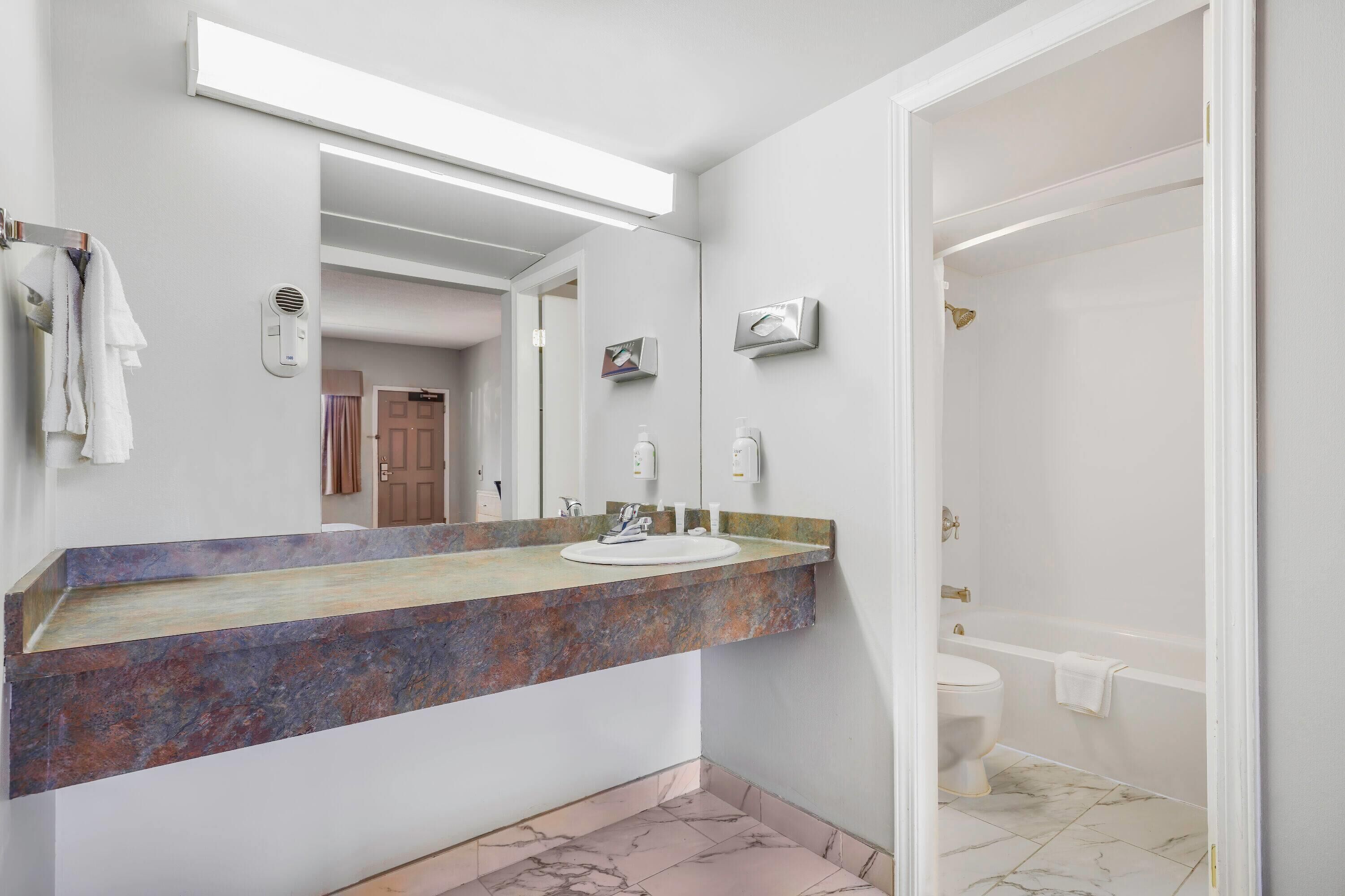 A bathroom with a marble sink, a large mirror, and a bathtub.