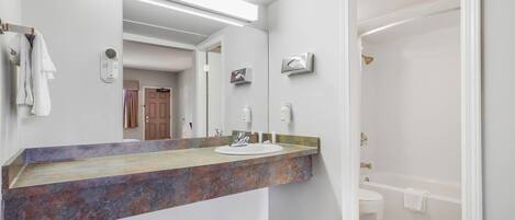 A bathroom with a marble sink, a large mirror, and a bathtub.