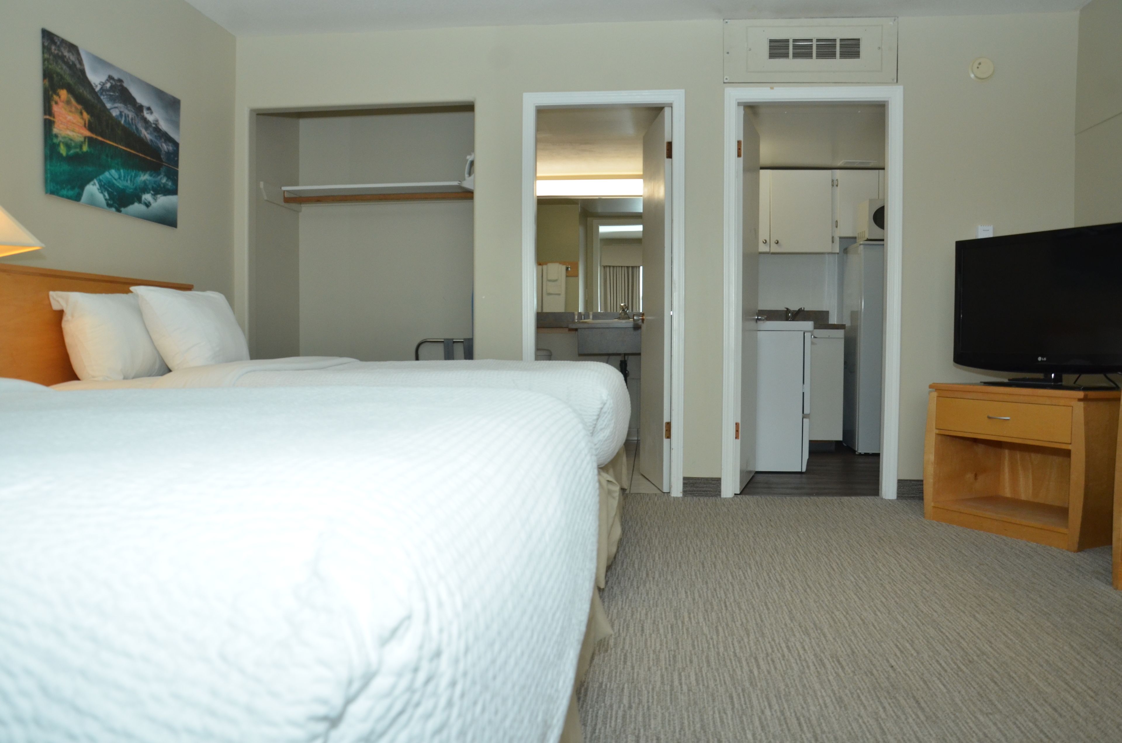 Une chambre d’hôtel comprenant un lit, une télévision, une petite armoire en bois et une kitchenette.