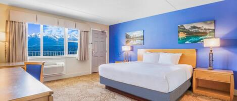 A hotel room with a large bed, two bedside tables, a desk, and a window with a mountain view.