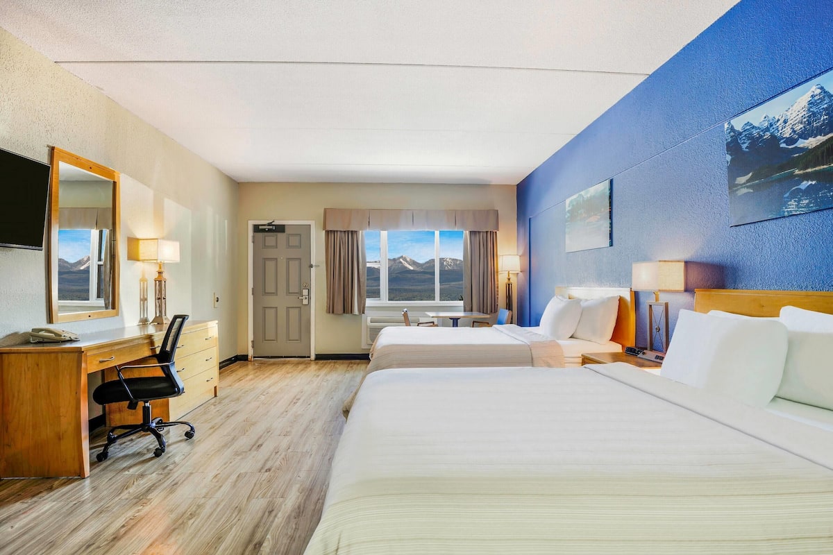 A hotel room with two beds, a desk, a chair, and a TV.