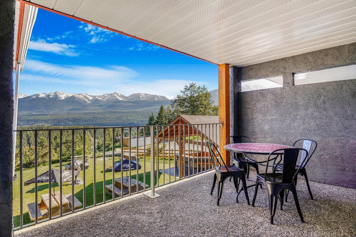 A balcony with a table and chairs, a view of mountains, and a wooden structure in the background.