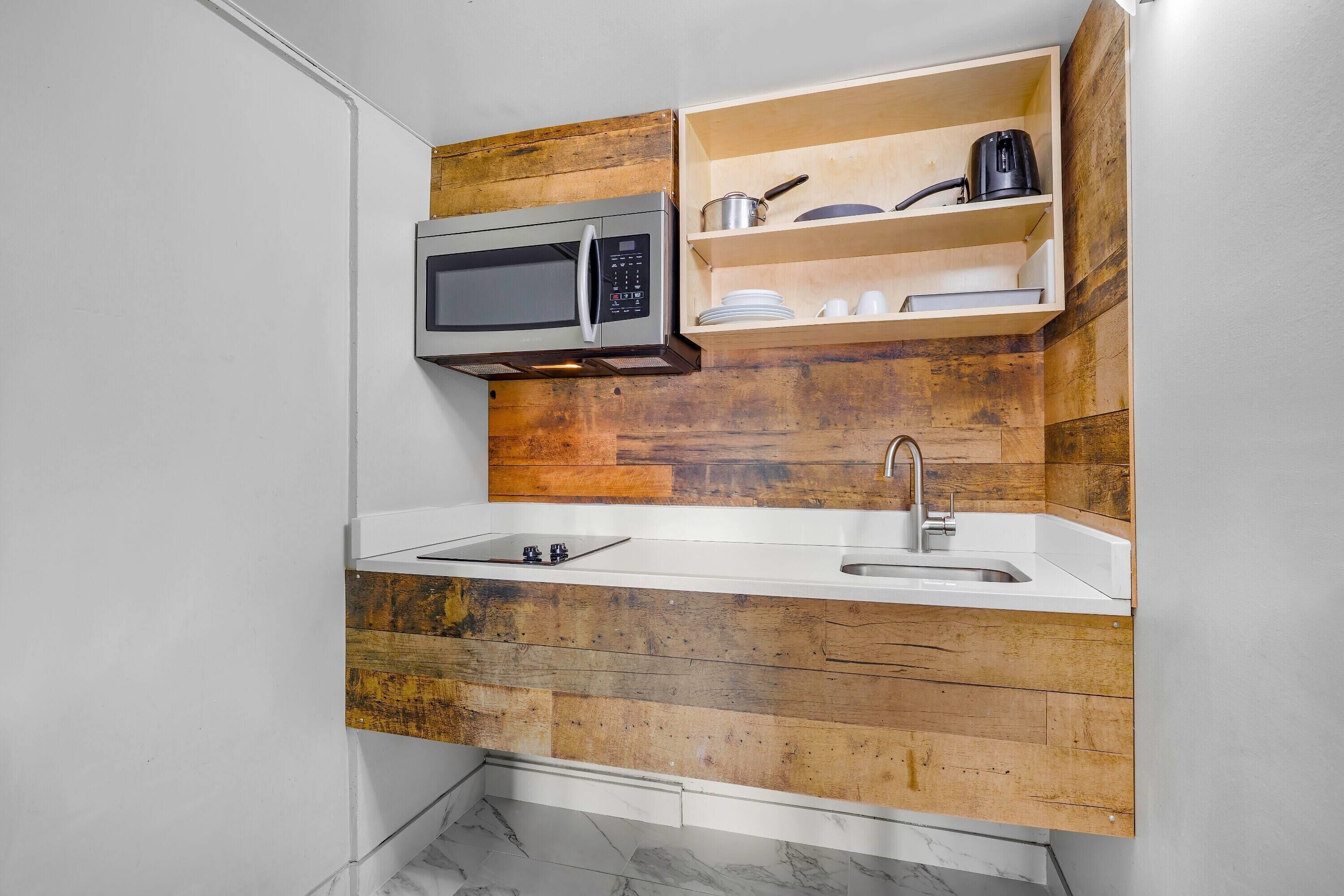 A compact kitchen with a built-in microwave, a sink, and wooden shelves.