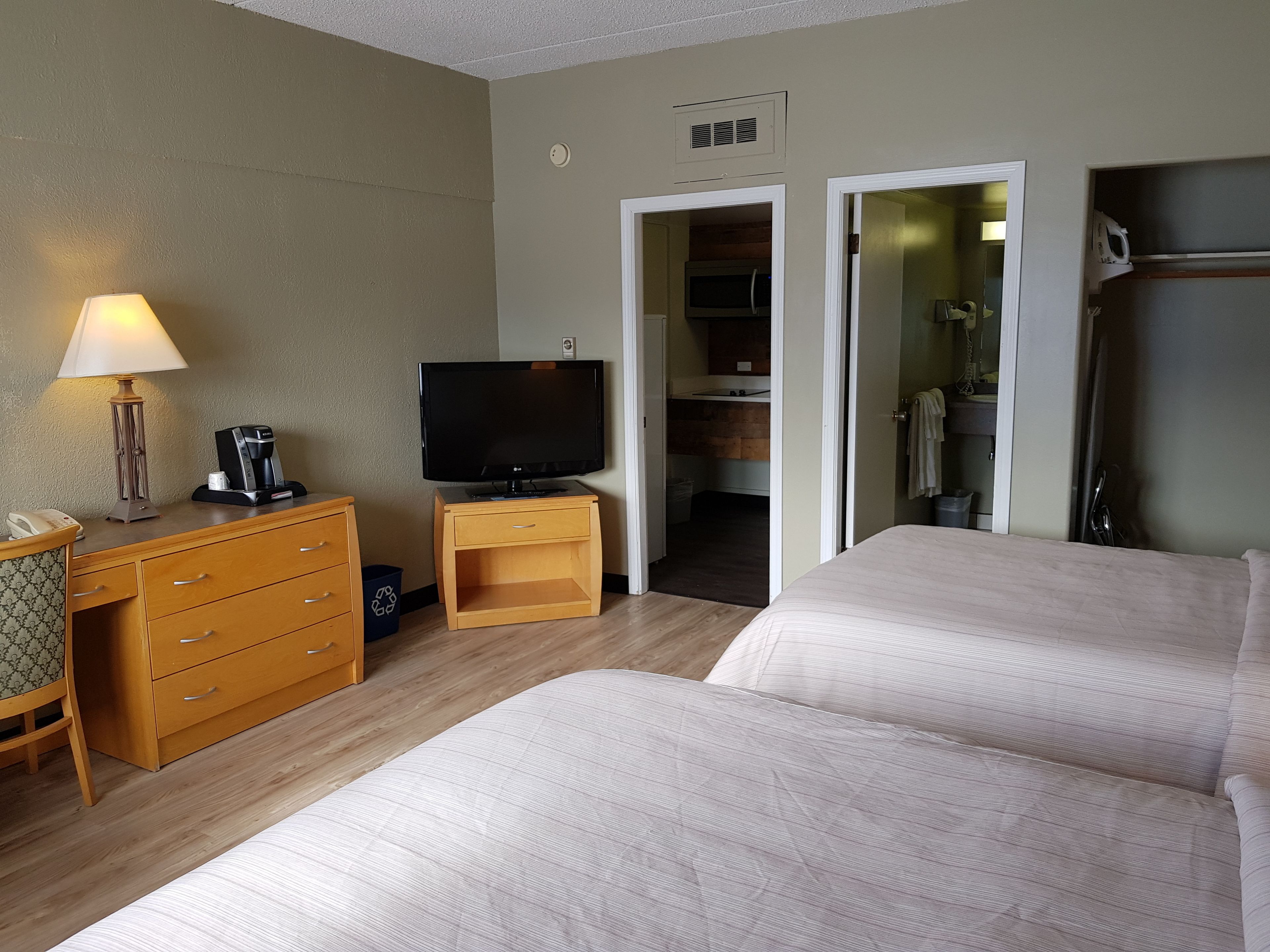 Une chambre d’hôtel avec deux lits, un bureau avec une lampe, une machine à café, une télévision et une salle de bain visible à travers une porte ouverte.