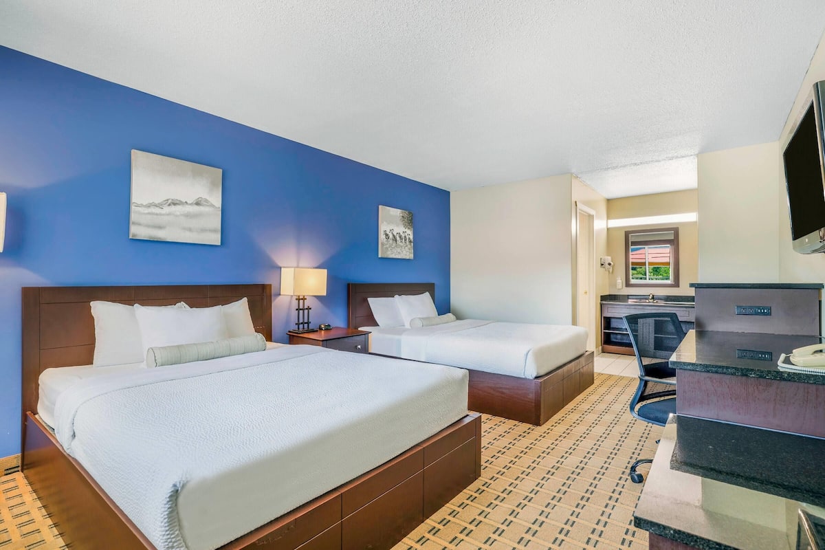 A hotel room with two beds, a desk, a chair, and a TV.