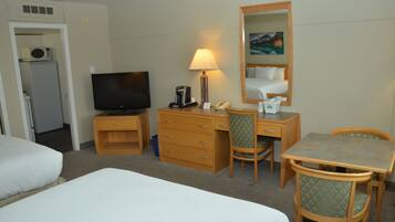 A hotel room with two beds, a desk with a lamp, a television, a microwave, and a small refrigerator.