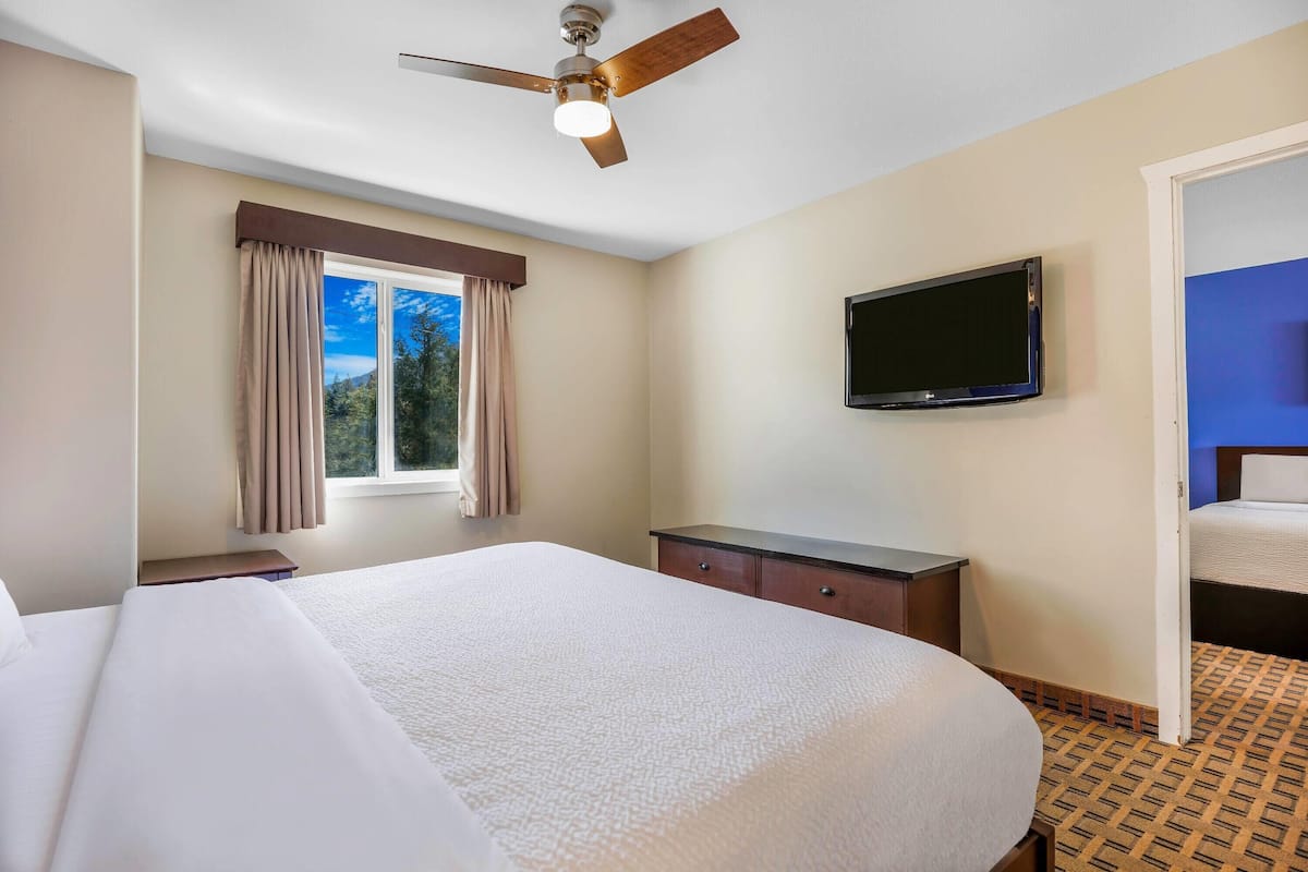 A hotel room with a large bed, a ceiling fan, a television, and a window with curtains.