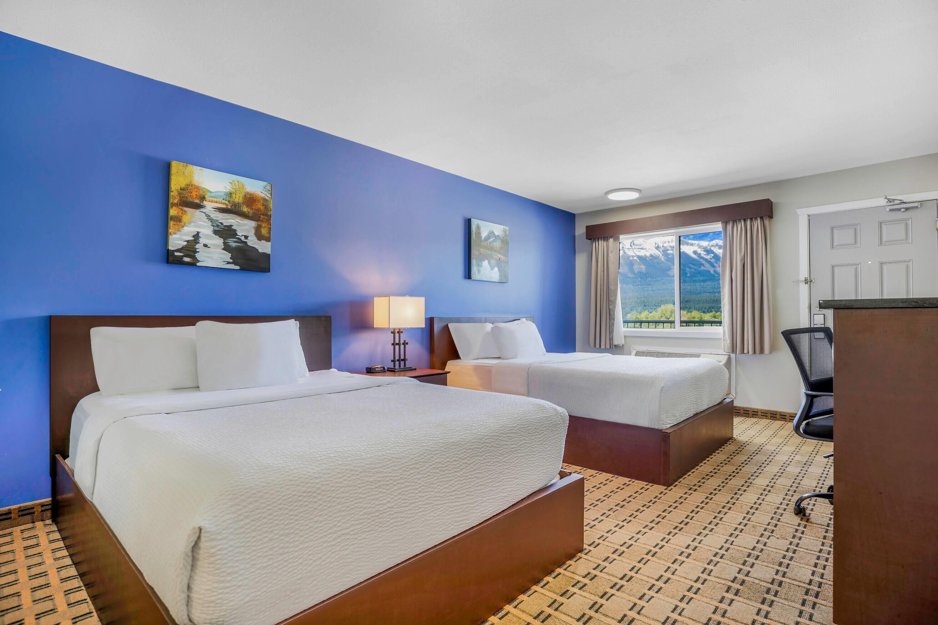 Une chambre d’hôtel avec deux lits, un bureau, une chaise, une lampe et un tableau au mur.