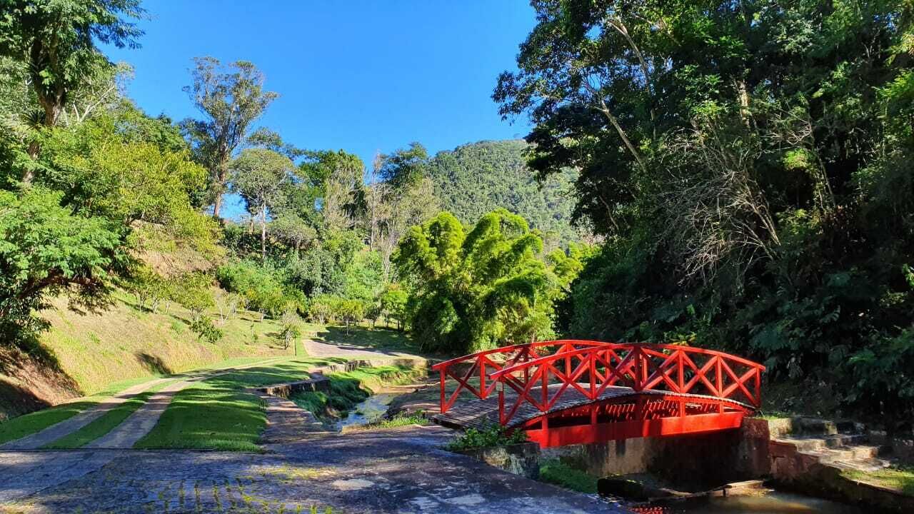 A red bridge over a water channel in a lush, green park with pathways and trees.