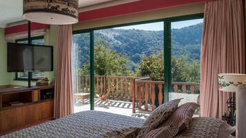A bedroom with a large bed, a TV, and a balcony with a view of a forested mountain.