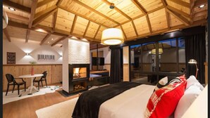 Un dormitorio amplio con una cama grande, una chimenea, un comedor con sillas y vistas al exterior a través de grandes ventanales.