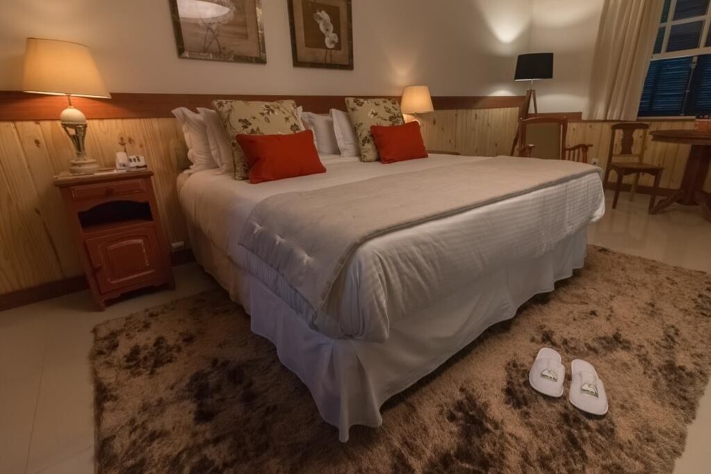 Un dormitorio ordenado con una cama grande, dos mesitas de noche con lámparas, un escritorio pequeño y una silla.