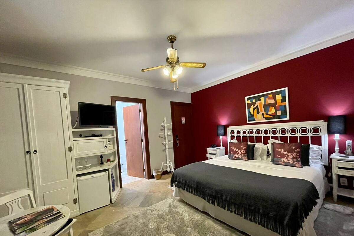 Ein Schlafzimmer mit Bett, Nachttischen, einem Fernseher, Deckenventilator und einer Tür zu einem anderen Raum.