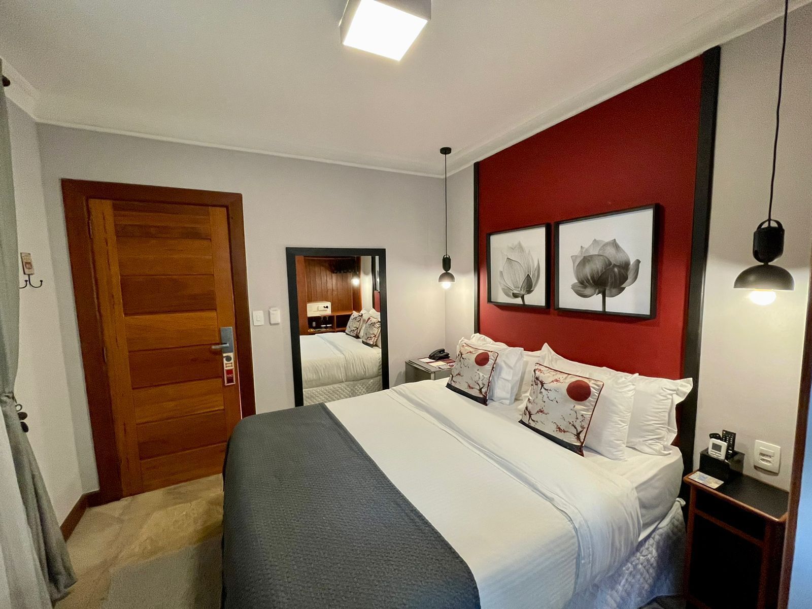 Habitación de hotel con una cama grande, una puerta de madera, un espejo y dos cuadros en la pared.