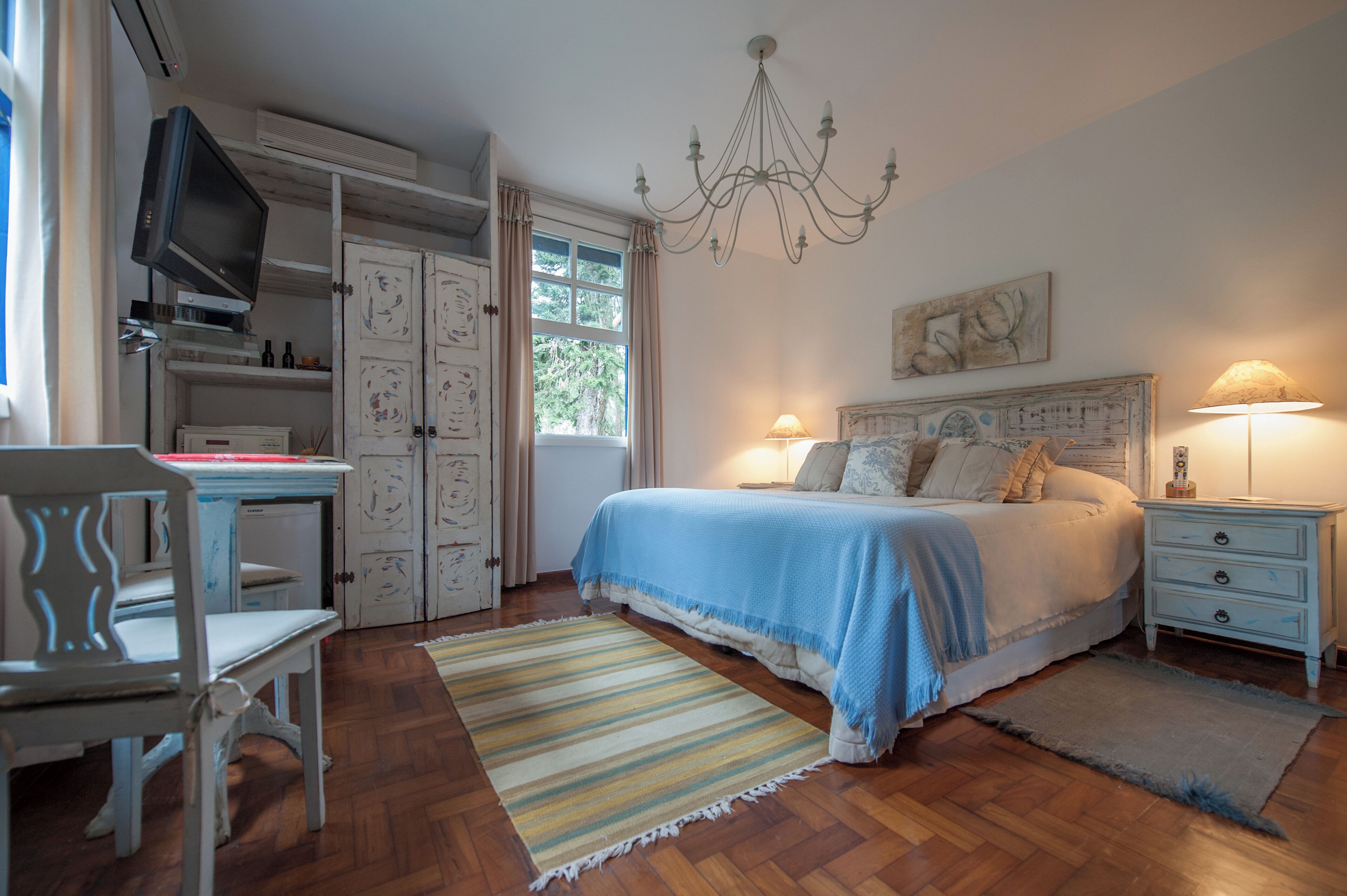 A bedroom with a bed, bedside tables, a TV, and a chandelier.