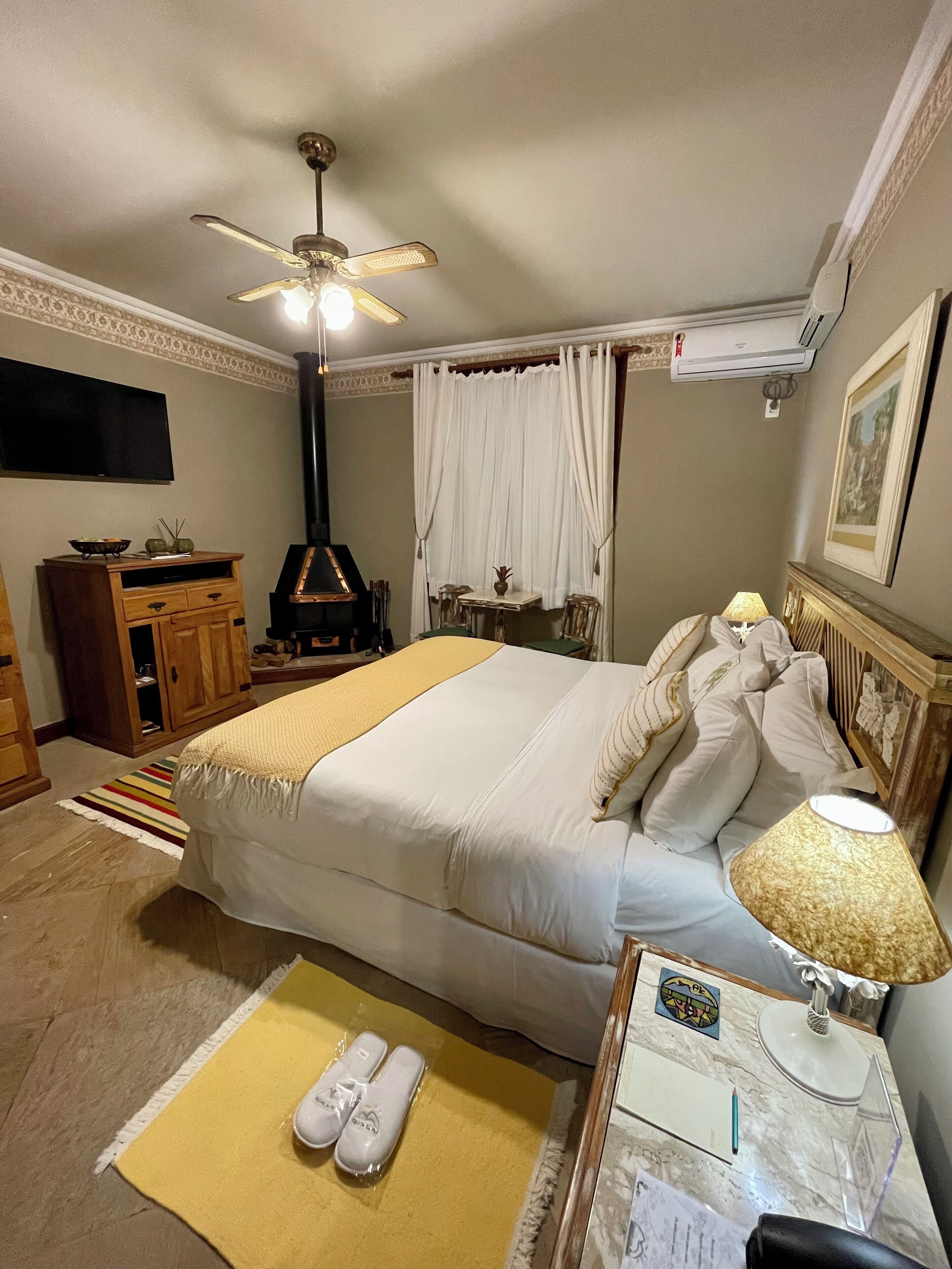 Een hotelkamer met een bed, een bureau met lamp, een televisie, een kledingkast en een open haard.