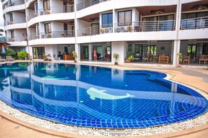 A hotel with a large swimming pool featuring a whale design, multiple balconies, and outdoor seating areas.